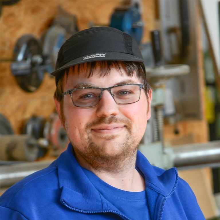 Ein Mann mit Brille und Hut lächelt in die Kamera.
