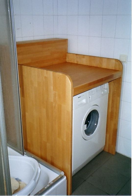 Eine Waschmaschine steht unter einer Holztheke in einem Badezimmer