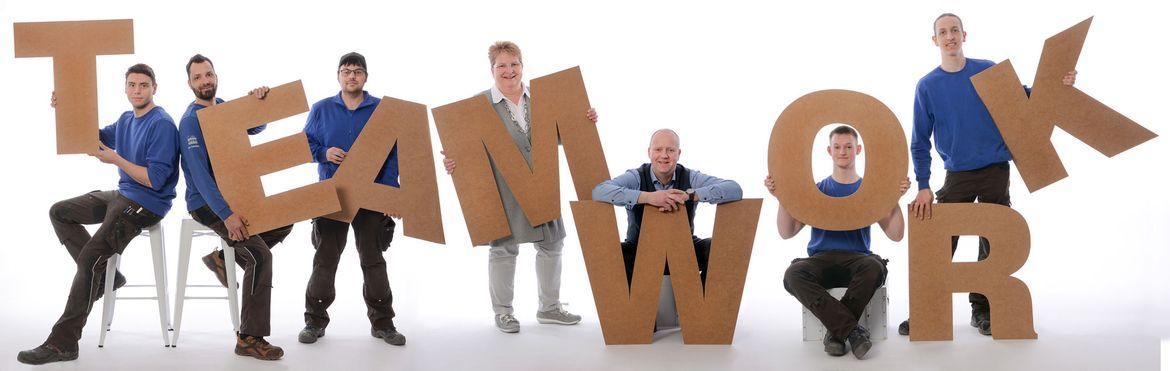 Eine Gruppe von Männern hält Pappbuchstaben hoch, die das Wort „Teamwork“ bedeuten.