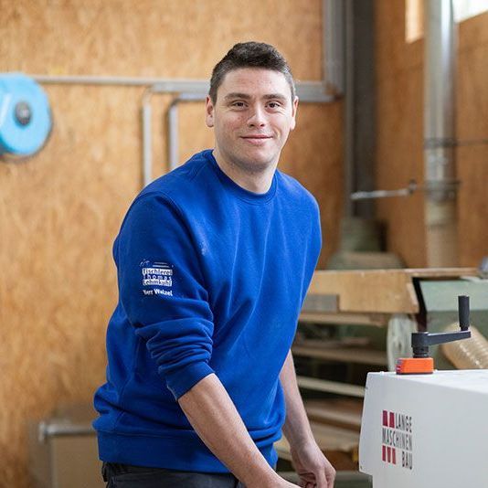 Ein Mann in einem blauen Pullover steht vor einer Maschine.