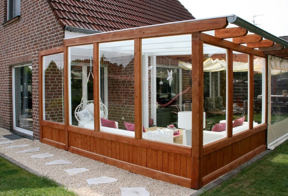 Ein Wintergarten aus Holz mit einem Backsteinhaus im Hintergrund