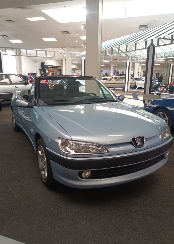 Voiture ancienne rouge garée au bord de l'océan, avec l'eau et le ciel bleus.
