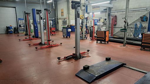 À l'intérieur d'un atelier de réparation automobile, sol rouge avec plusieurs ponts élévateurs.
