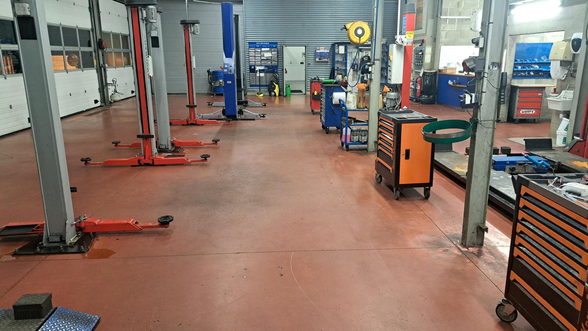 Un atelier de réparation automobile avec plusieurs ponts élévateurs, des outils et un sol rouge.