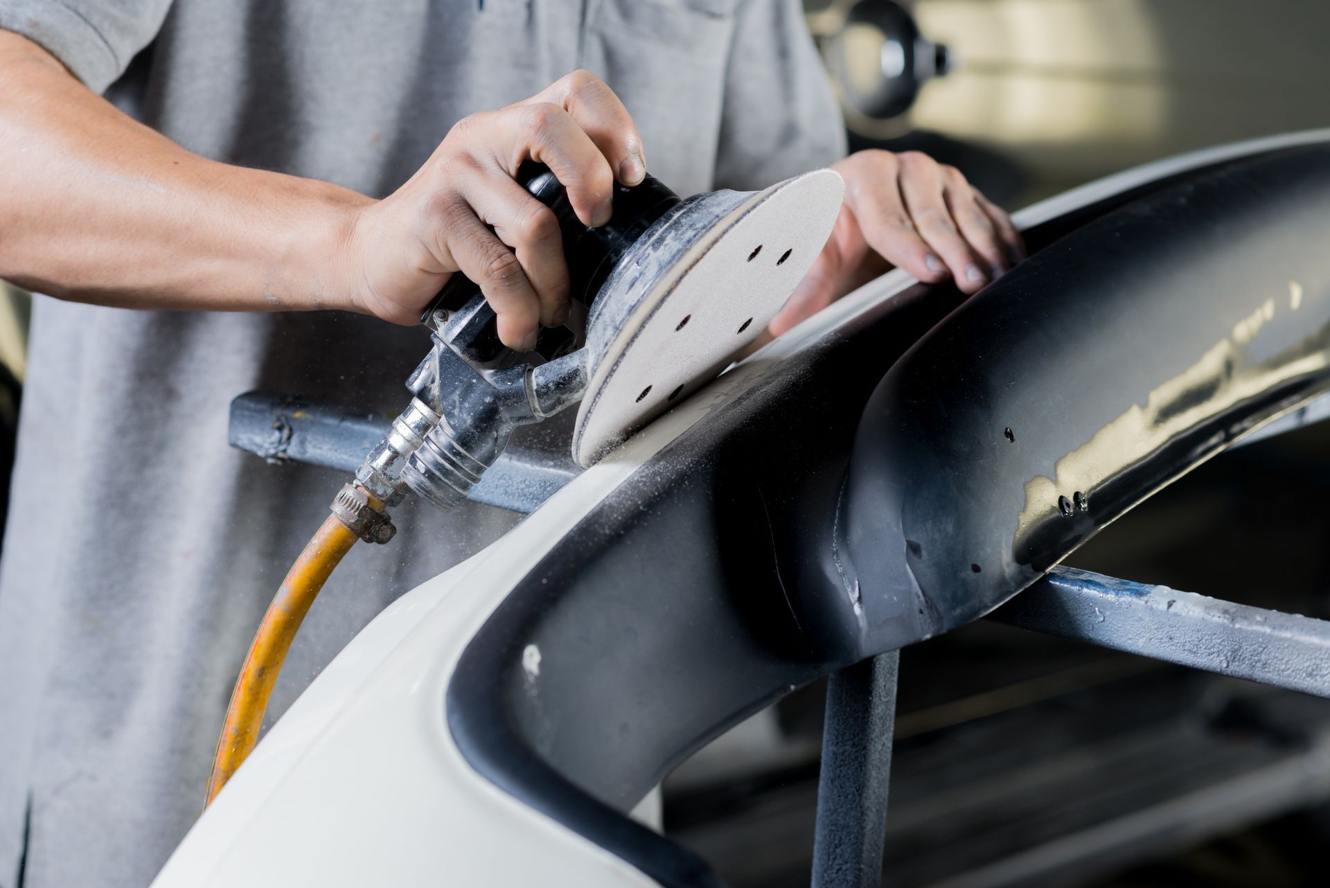 Une personne polit le pare-chocs d'une voiture rouge avec un tampon bleu, sous un capot partiellement ouvert.