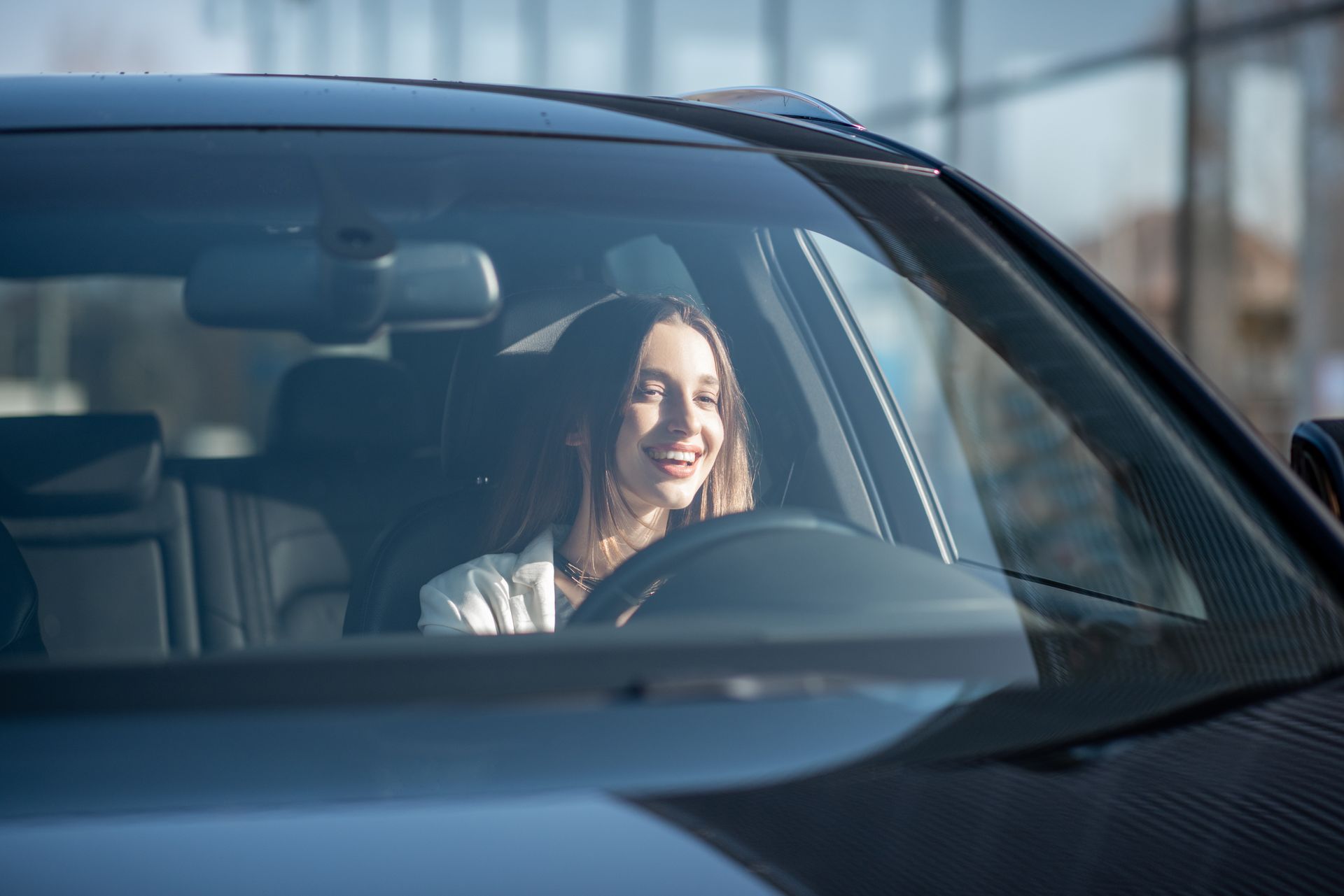 Une femme sourit dans une voiture, regardant à travers le pare-brise. Intérieur et extérieur d'une voiture noire.