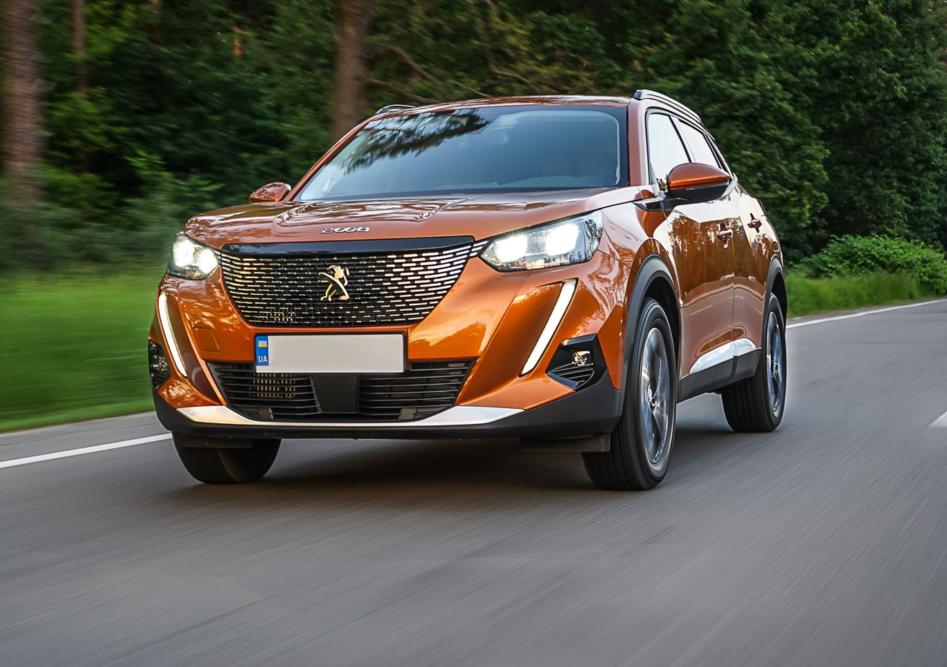 Un SUV Peugeot 2008 orange circule sur une route avec des arbres en arrière-plan.