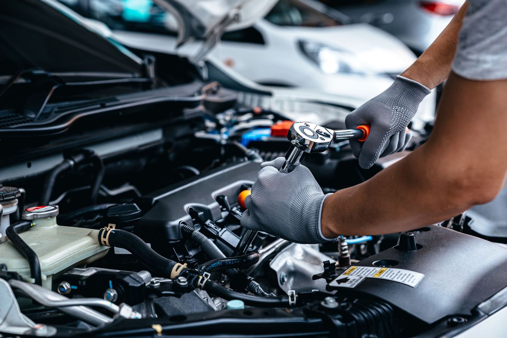 Un mécanicien utilise une clé pour travailler sur le moteur d'une voiture, portant des gants, dans un garage.