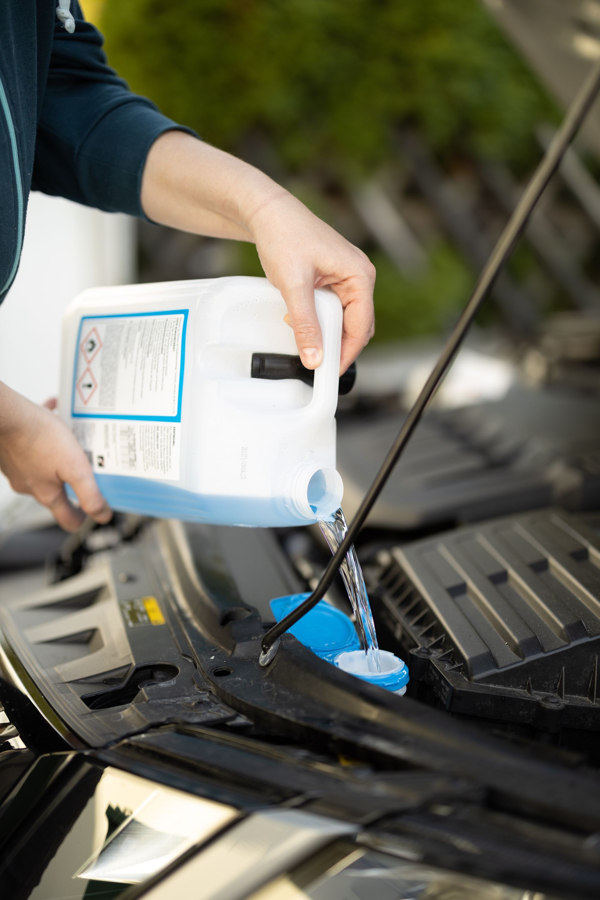 Une personne verse du liquide lave-glace bleu dans le réservoir situé sous le capot d'une voiture.