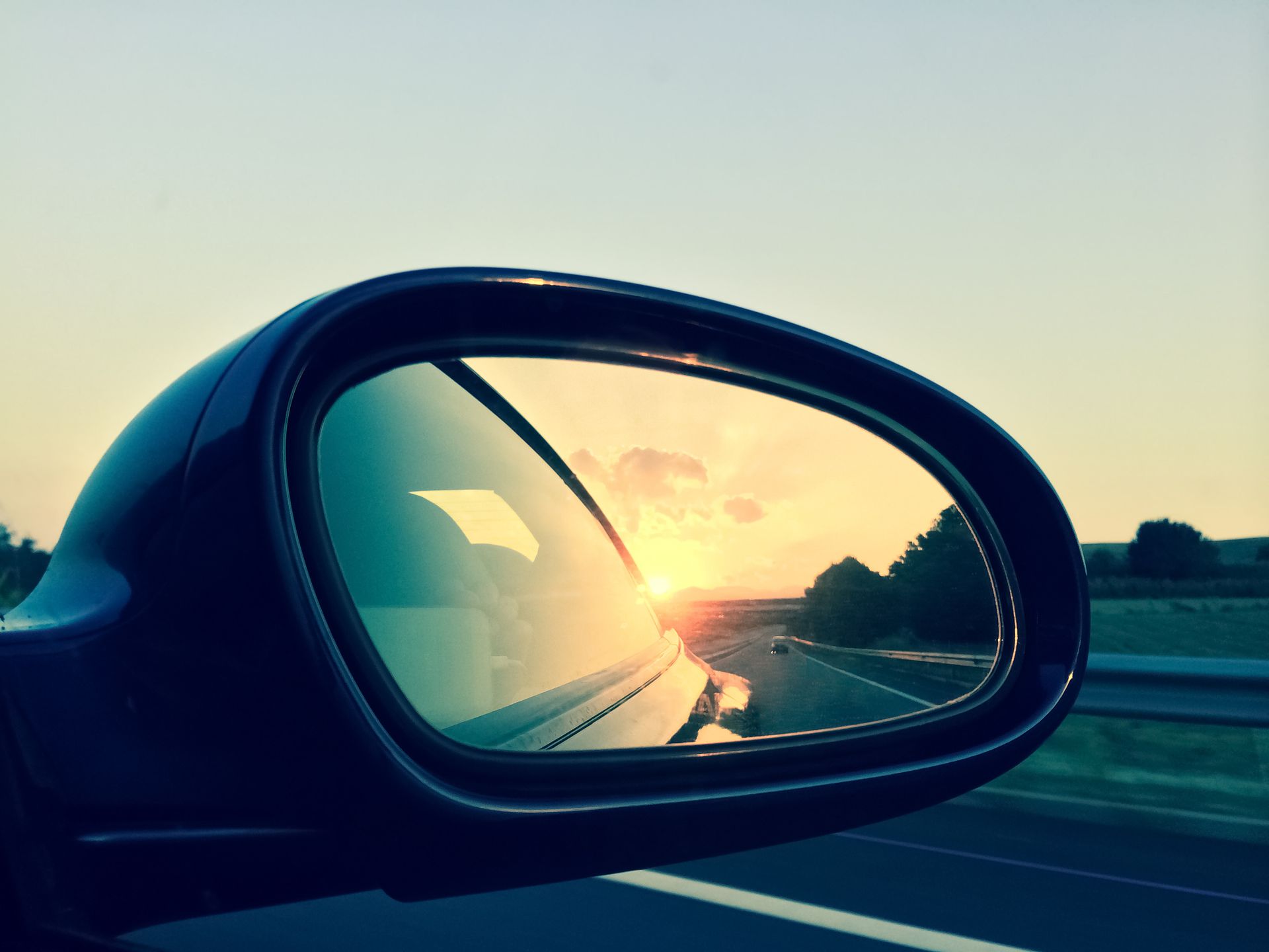 Le reflet du soleil couchant dans le rétroviseur d'une voiture ; autoroute, soleil éclatant et voiture bleue.