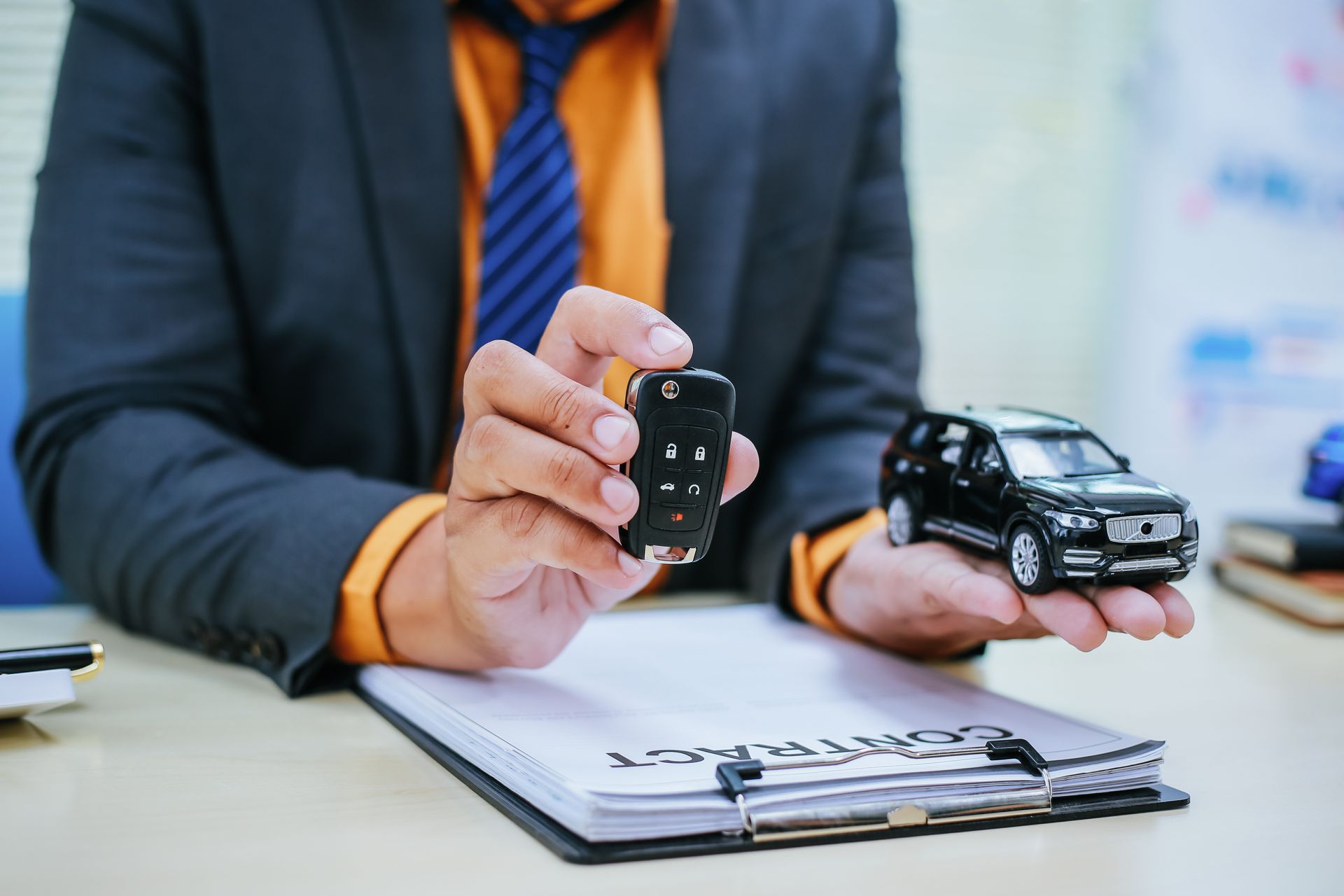 Un homme en costume tient une clé de voiture et une voiture miniature au-dessus du contrat.