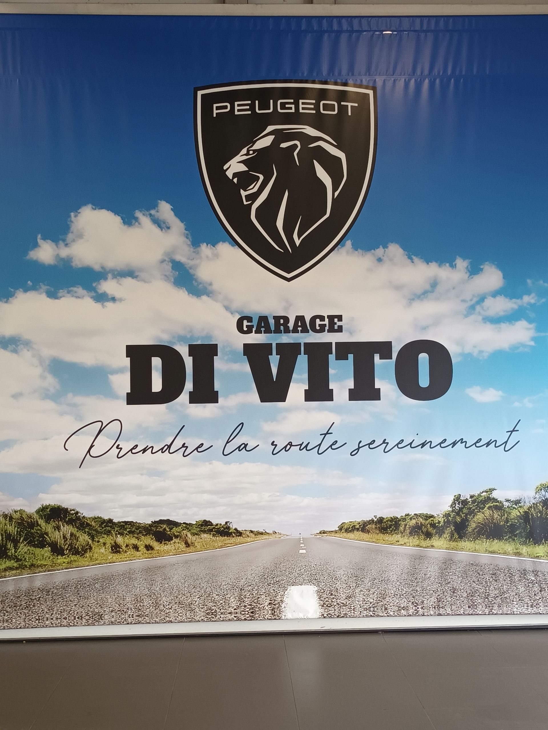 Une enseigne Peugeot pour Garage Di Vito, se détachant sur un ciel bleu et une route.