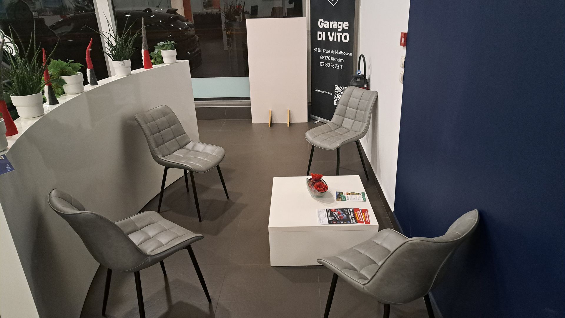 Salle d'attente avec chaises grises, table blanche avec objets et mur bleu marine.