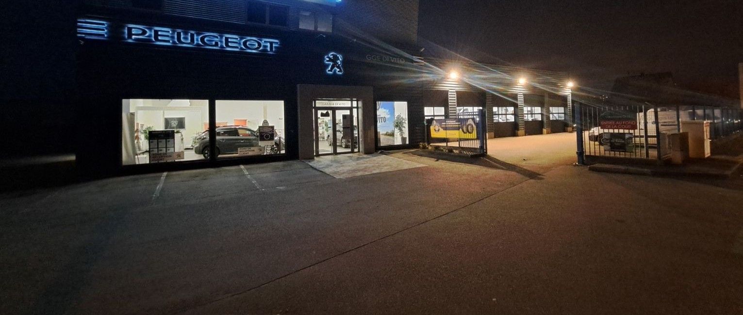Concessionnaire Peugeot la nuit, avec logo et façade illuminés.