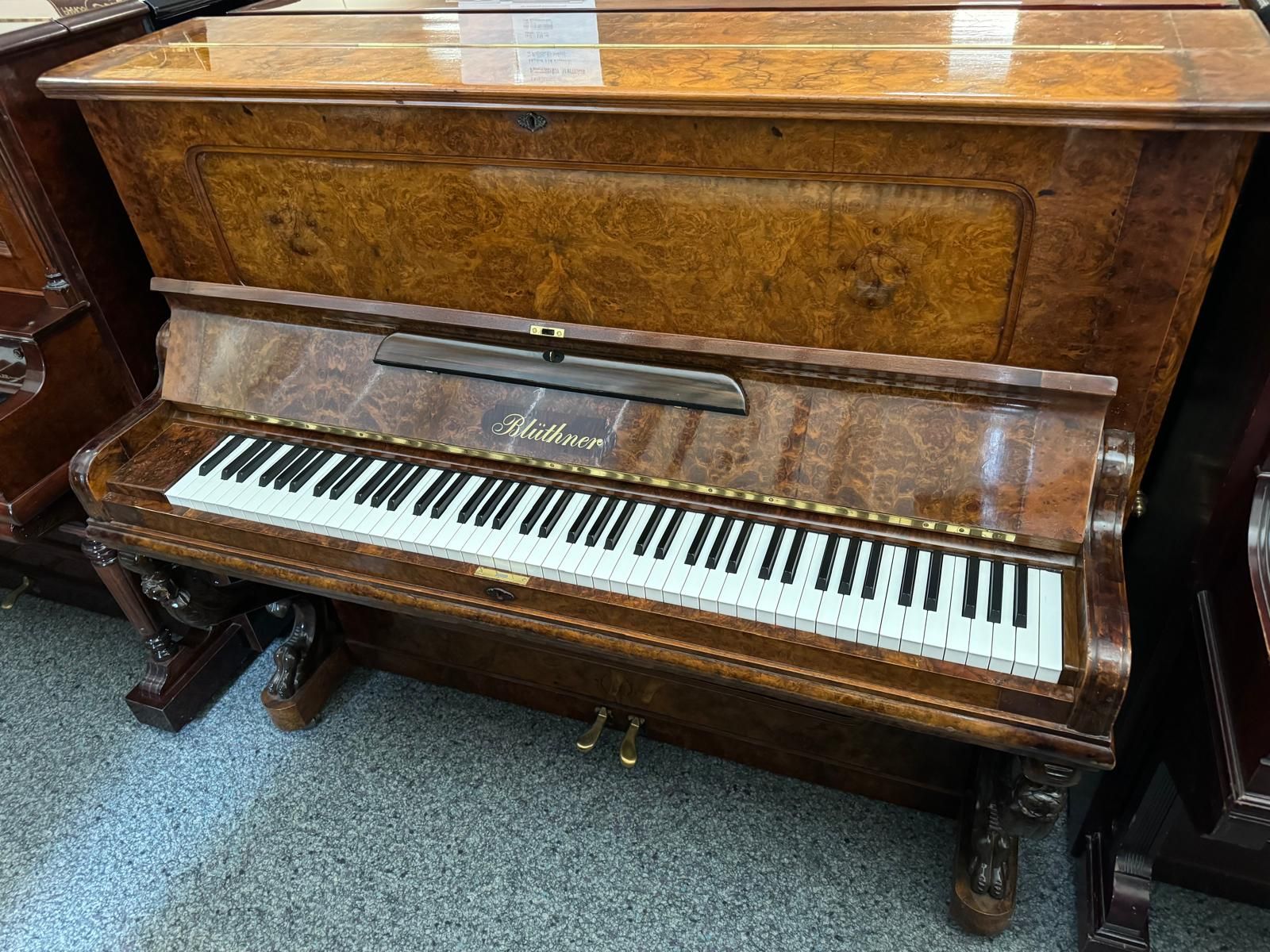 Ein hölzernes Klavier steht in einem Raum mit anderen Klavieren.