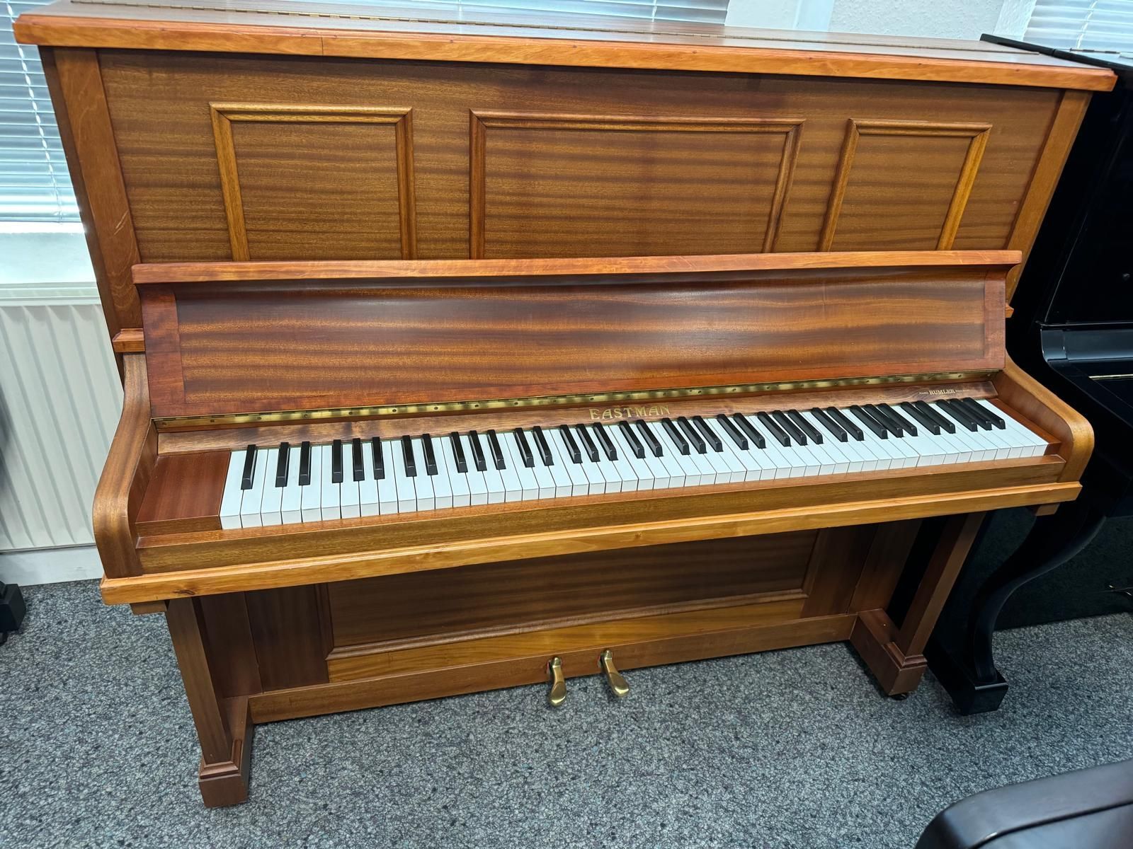 Ein hölzernes Klavier steht in einem Raum mit anderen Klavieren.