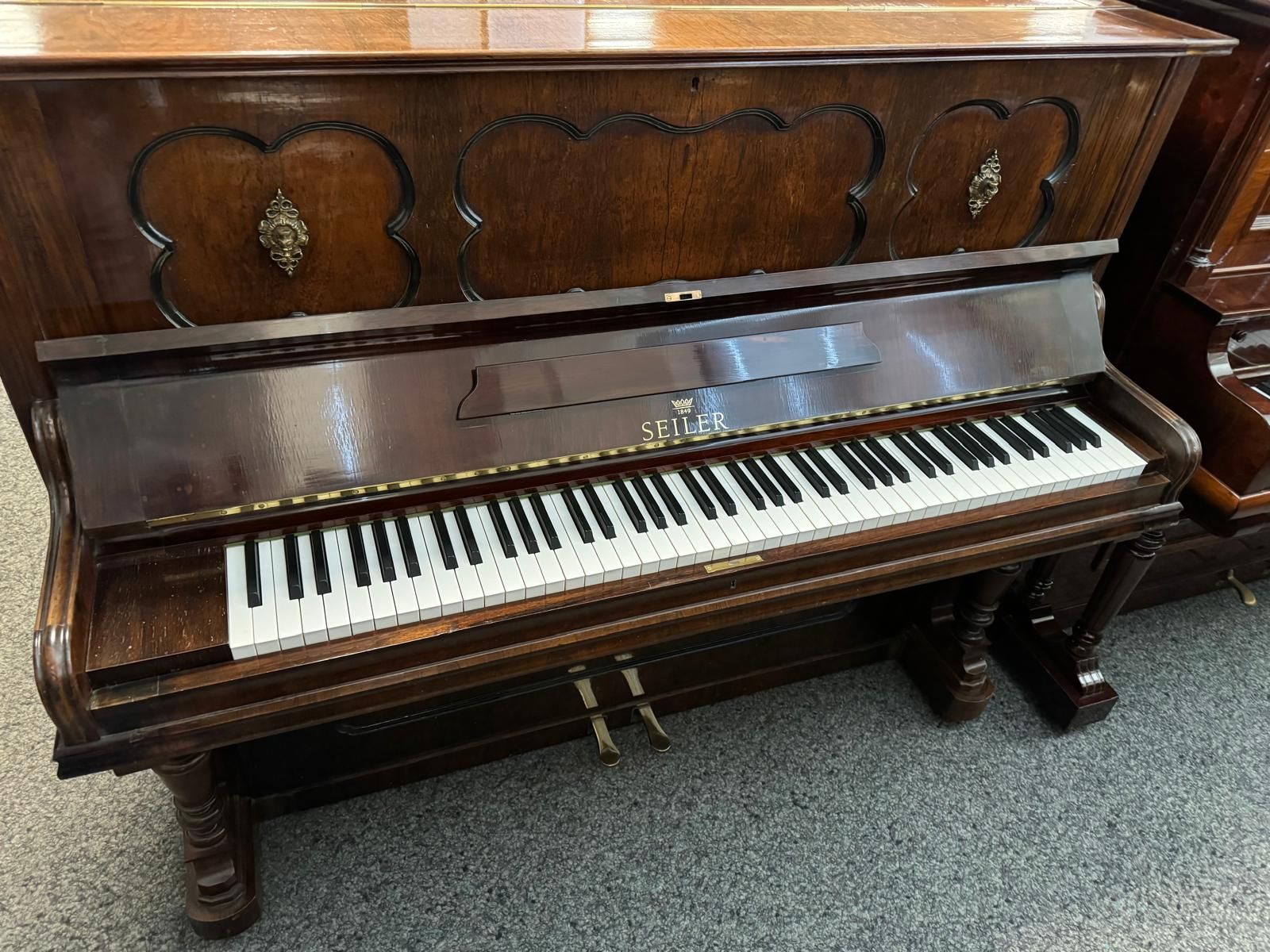 Ein hölzernes Klavier steht in einem Raum mit anderen Klavieren.