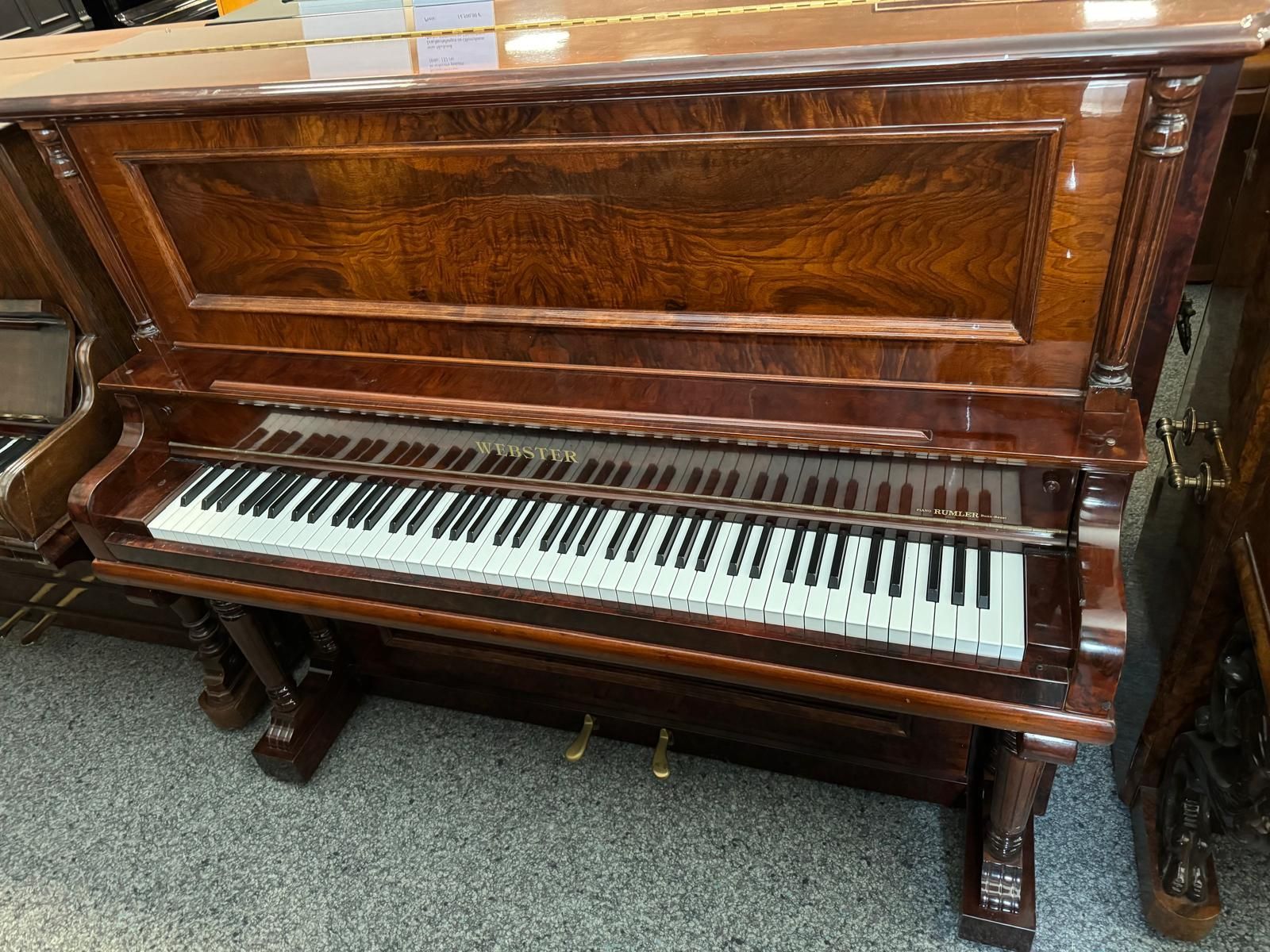 Ein hölzernes Klavier steht in einem Raum mit anderen Klavieren.