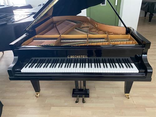 Ein schwarzer Flügel steht auf einem Holzboden.