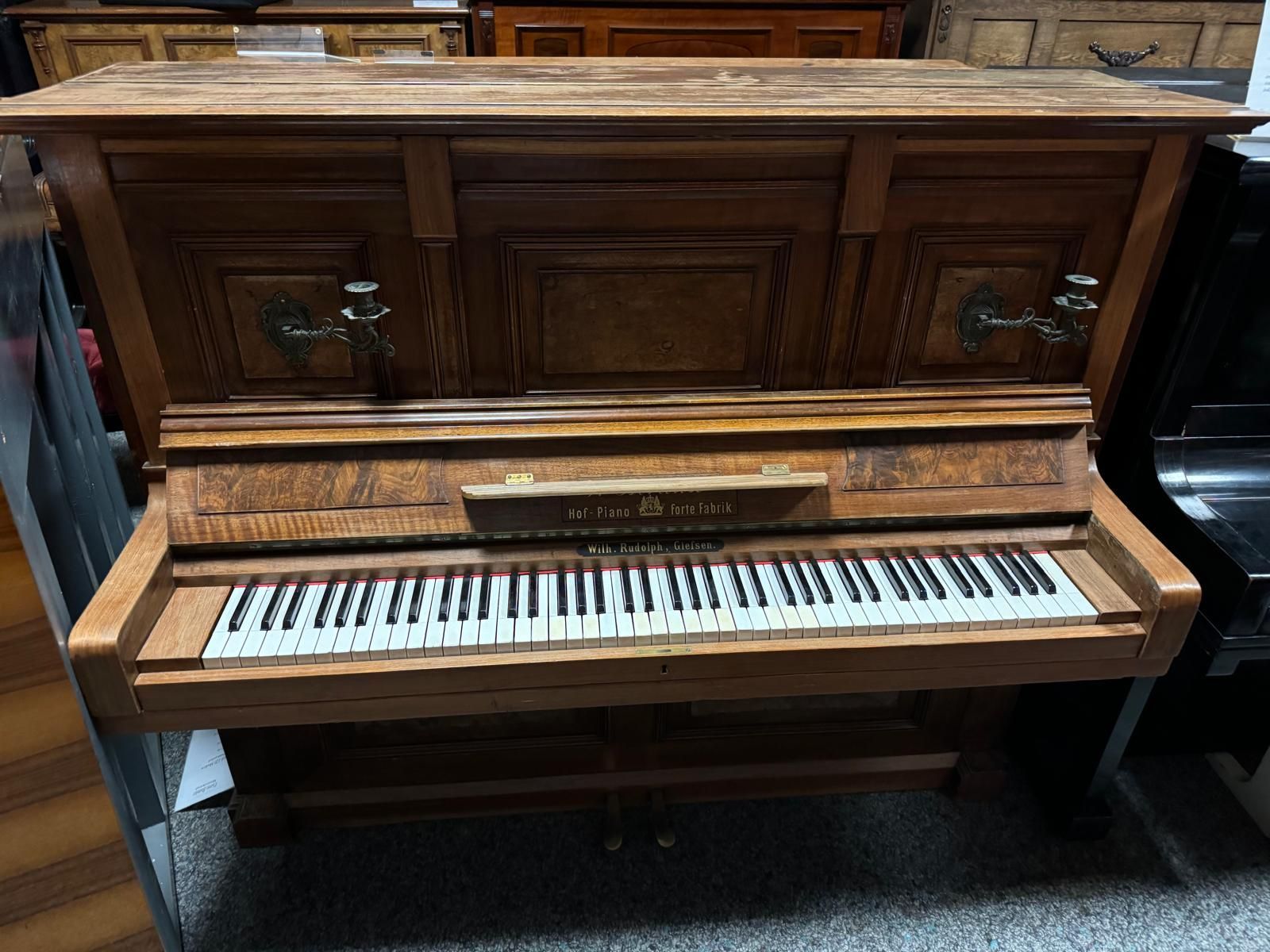 Ein hölzernes Klavier steht in einem Raum mit anderen Klavieren.