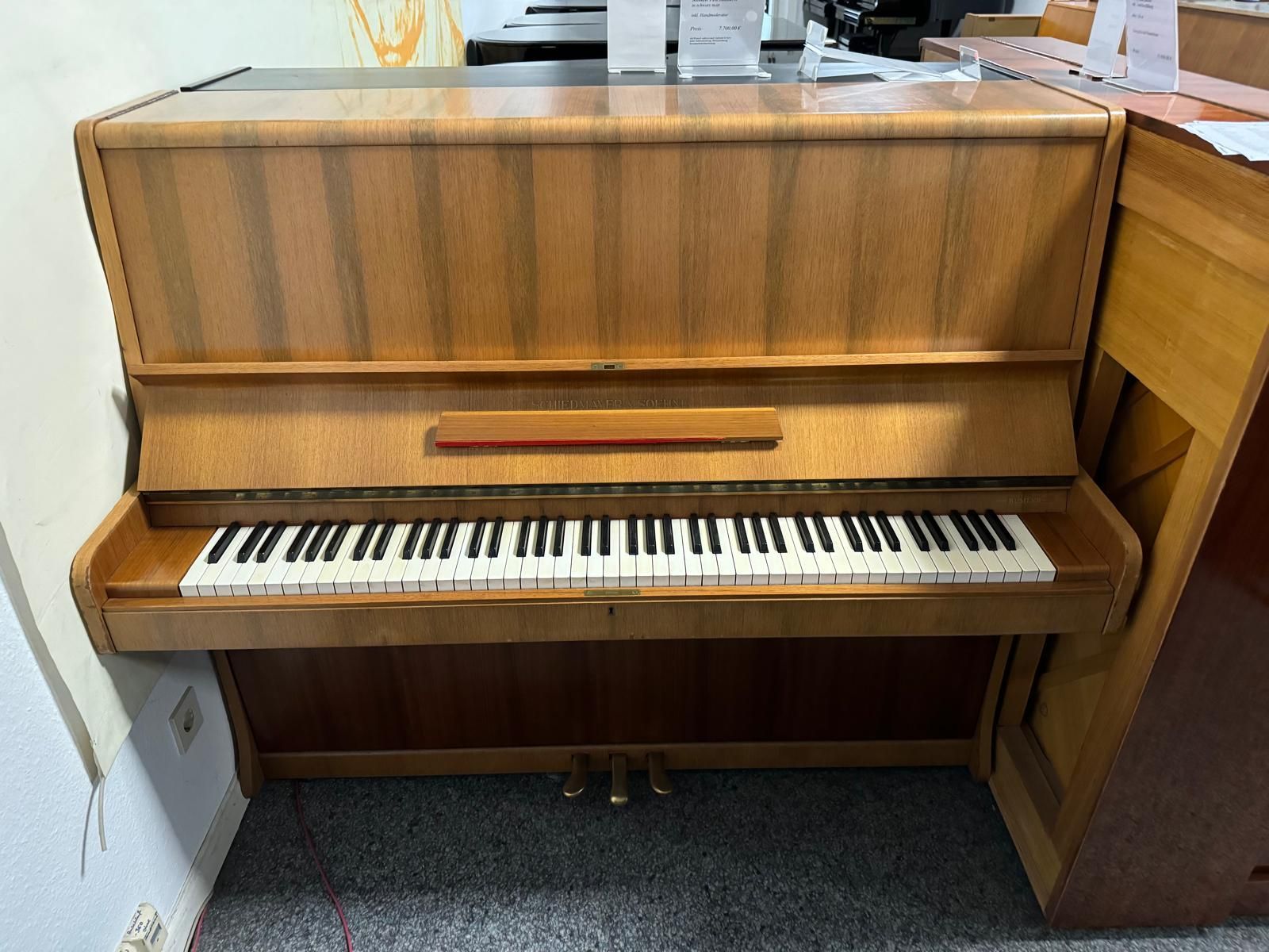 Ein hölzernes Klavier steht in einem Raum mit anderen Klavieren.