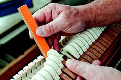 Eine Person arbeitet mit einem Lineal an einem Klavier.