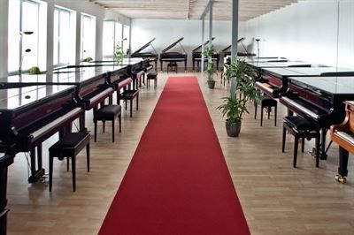 In einem Raum mit einem roten Teppich steht eine Reihe Klaviere.