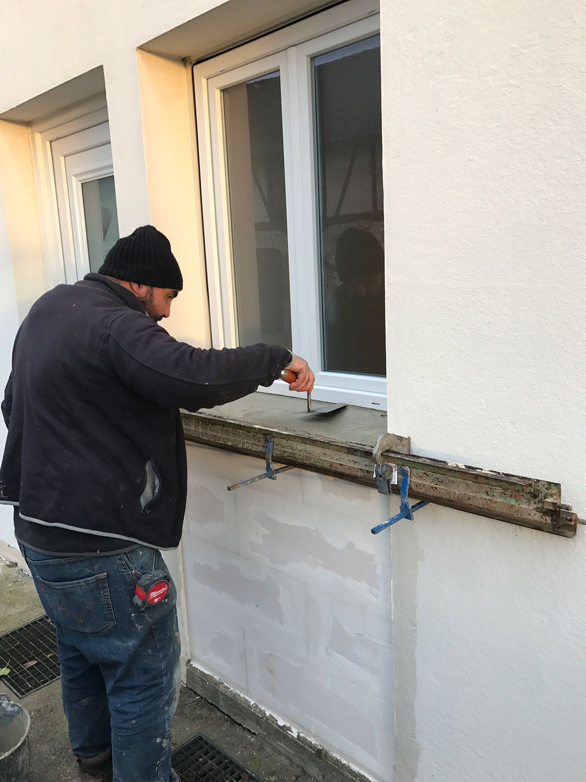 Artisan qui étale du ciment au bord d'une fenêtre.