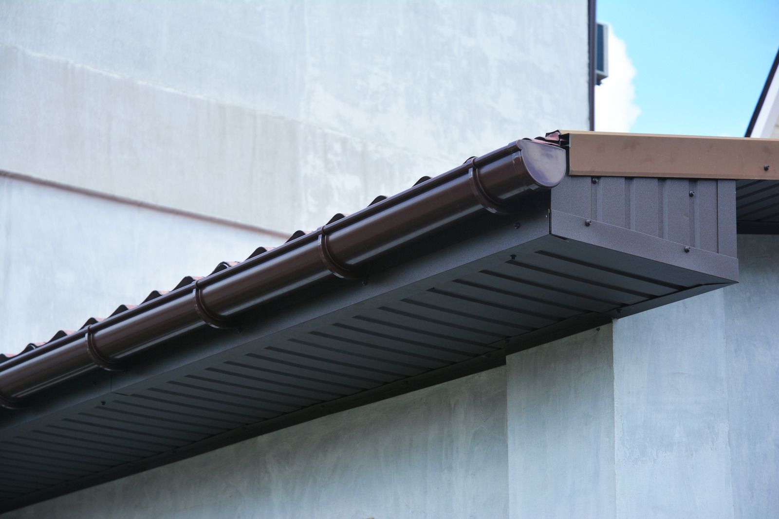 Close-up of a dark brown roof gutter and downspout on a light blue building wall
