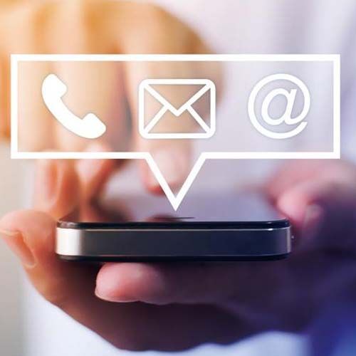 Una persona sostiene un teléfono celular con una burbuja de diálogo con los íconos de teléfono, correo electrónico y @.