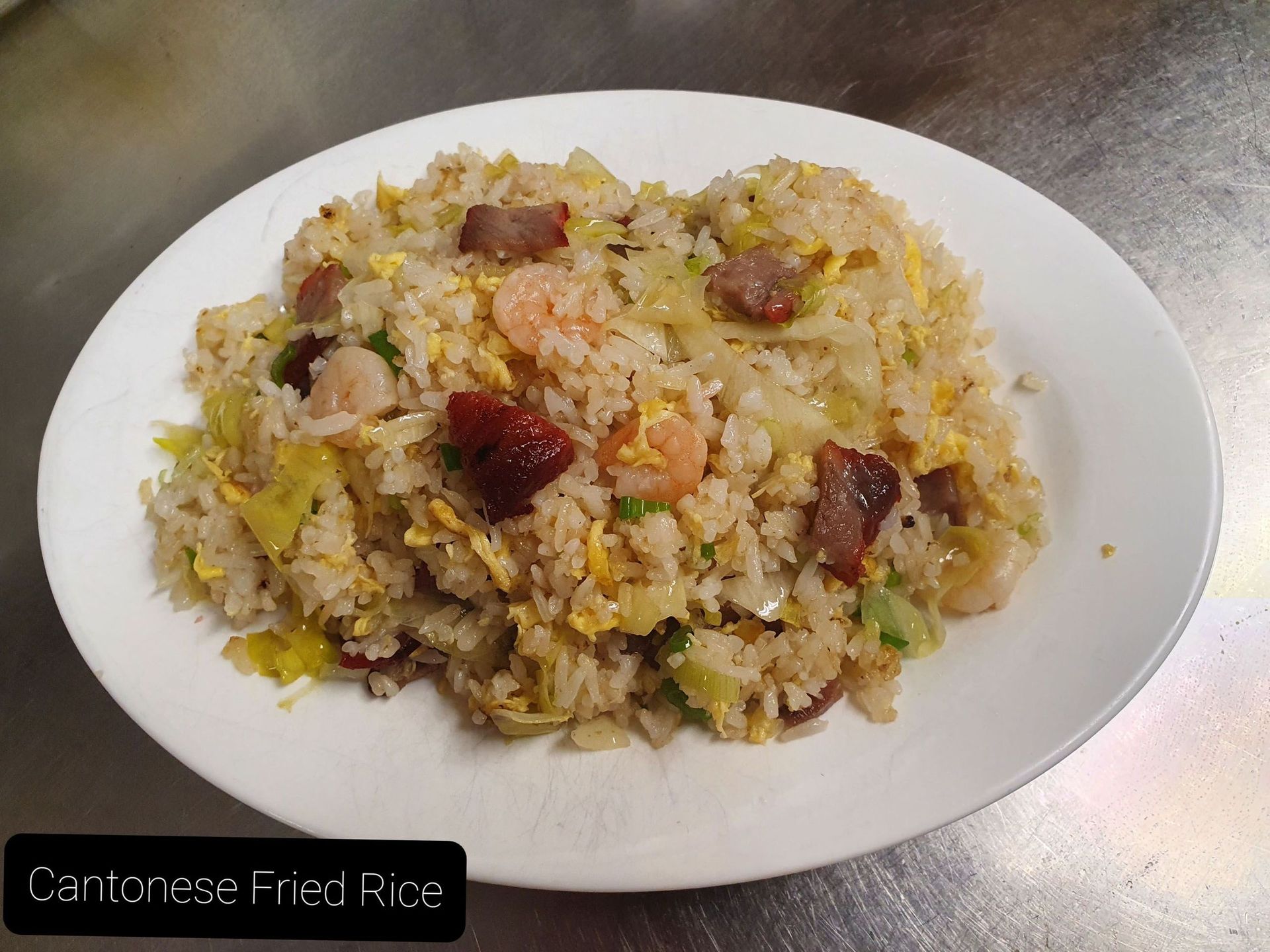 Ein weißer Teller mit gebratenem Reis und Fleisch auf einem Tisch.