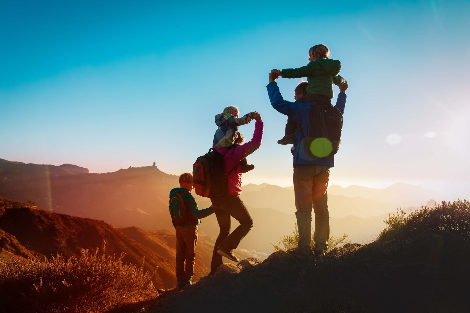 Une famille se découpe en silhouette sur un coucher de soleil doré, sur une crête montagneuse.