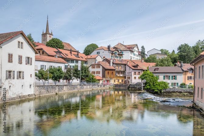 Une rivière s'écoule par-dessus un petit barrage de pierre vers un village niché au pied d'une montagne.