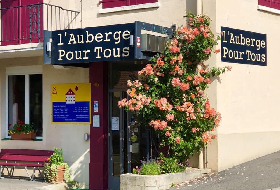 Un immeuble beige à plusieurs étages, aux volets bruns, se dresse dans un paysage vallonné.
