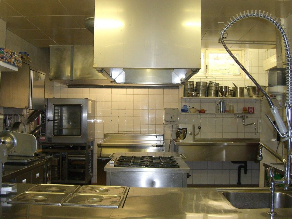 Cuisine professionnelle avec cuisinière à gaz centrale, hotte aspirante, comptoirs en acier inoxydable, four et évier.