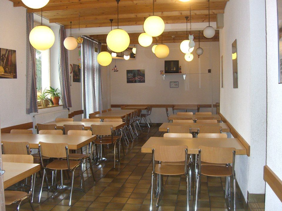 Une salle à manger intérieure avec des tables et des chaises en bois clair, un sol carrelé.