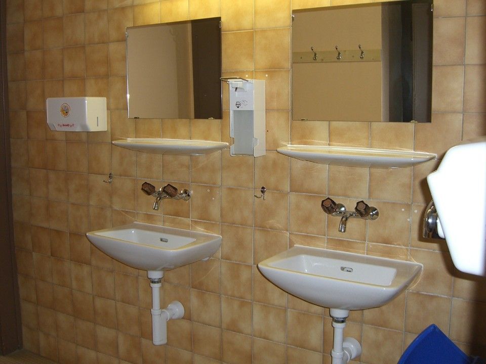 Des toilettes publiques avec deux lavabos blancs muraux, des miroirs rectangulaires, des étagères.
