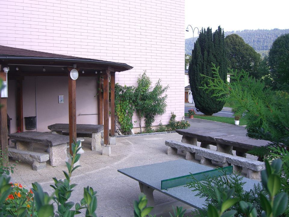 Une cour intérieure avec une table de ping-pong, des bancs en pierre et une pergola en bois couverte, adossée à un mur rose.