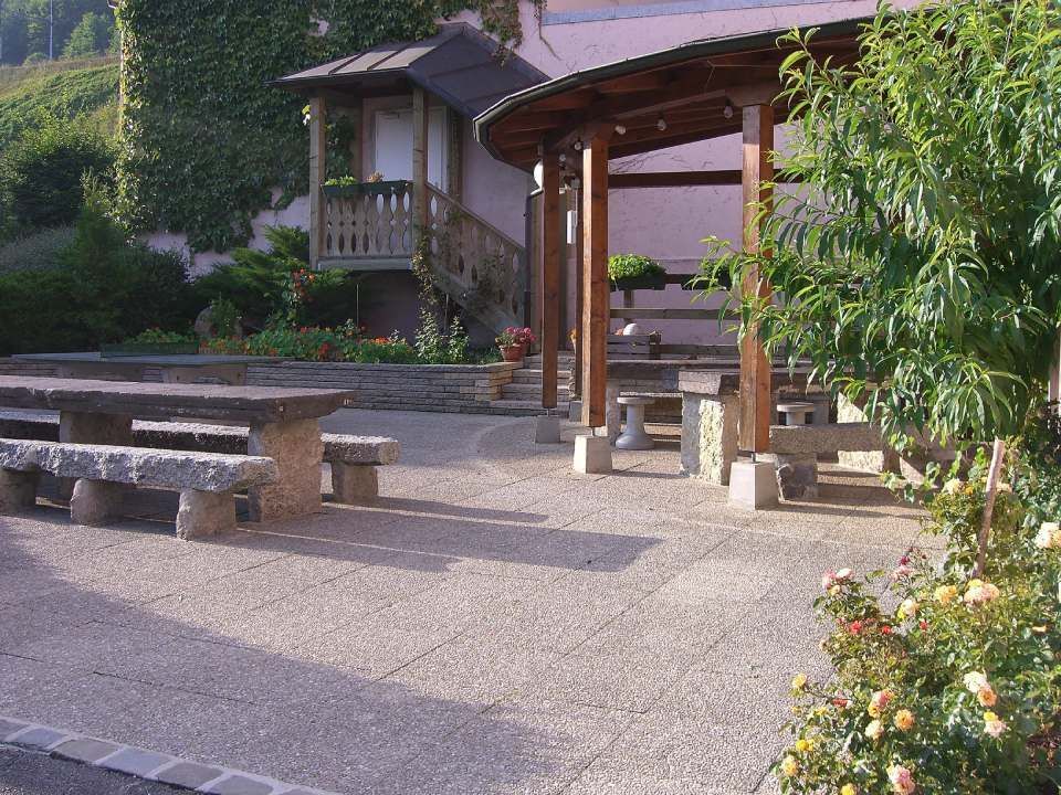 Une terrasse en pierre avec un kiosque en bois et des bancs en pierre assortis, entourée d'aménagements.