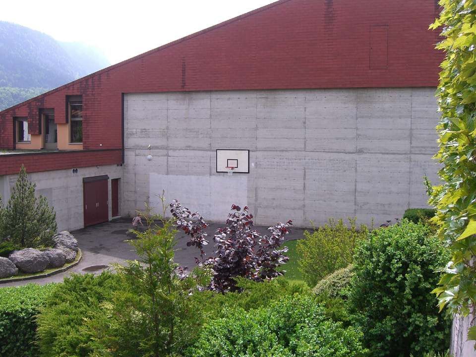 Un mur en béton avec un panier de basket-ball fixé dessus, se détachant sur un bâtiment rouge.