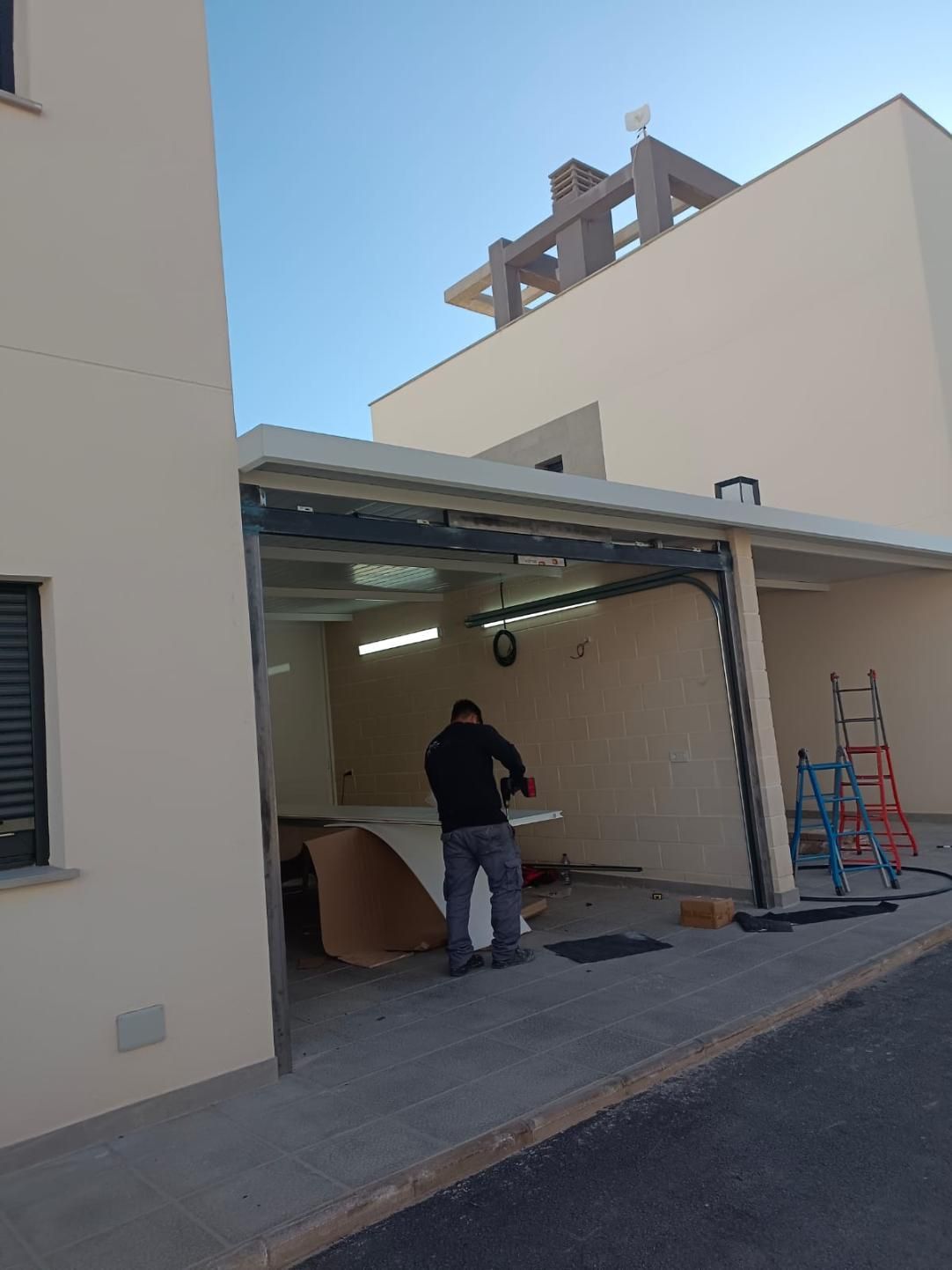 Hombre trabajando bajo una cochera. El edificio tiene un exterior claro y un cielo azul.