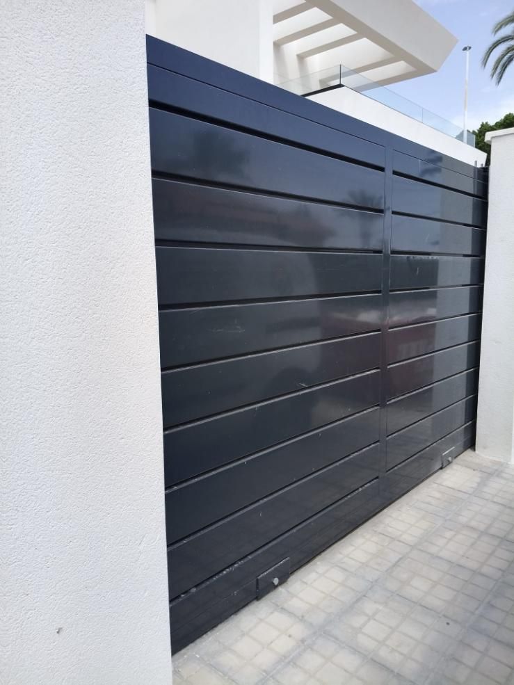 Puerta corredera de lamas horizontales de color gris oscuro junto a una pared de estuco blanco.