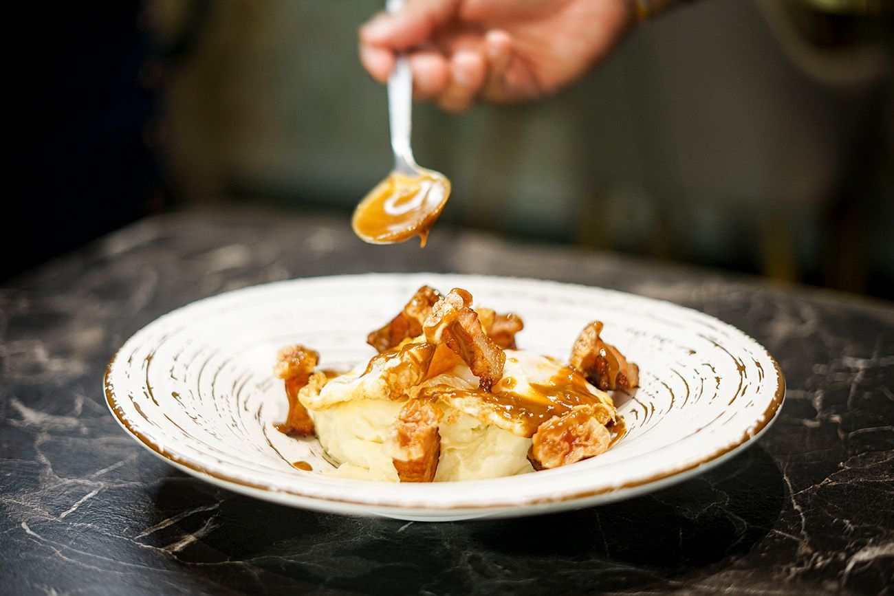 Una persona está vertiendo salsa en un plato de comida con una cuchara.