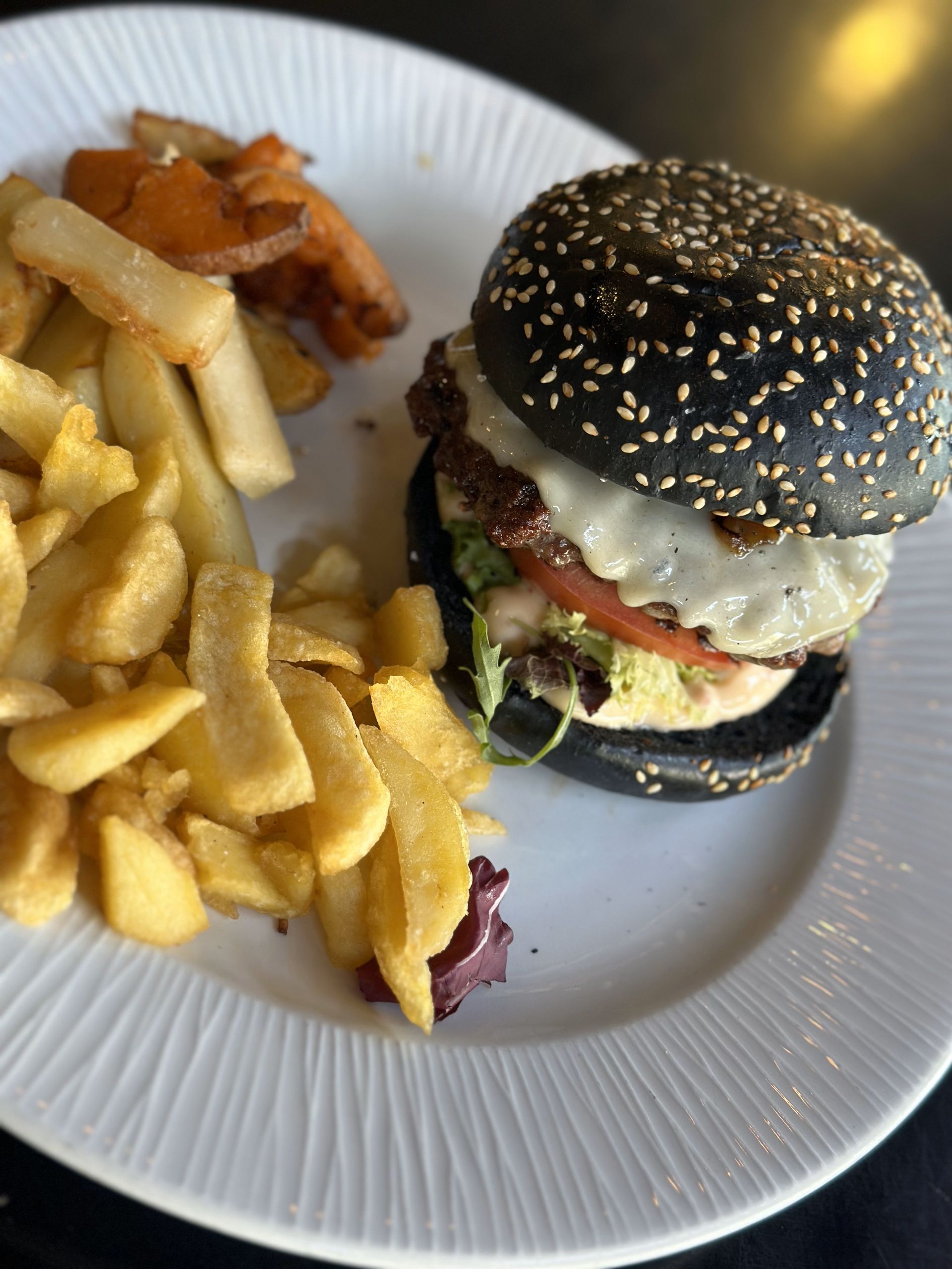 Un plato blanco cubierto con una hamburguesa negra y papas fritas.