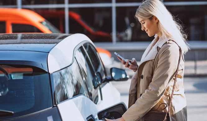 Una mujer está cargando su coche eléctrico y mirando su teléfono.