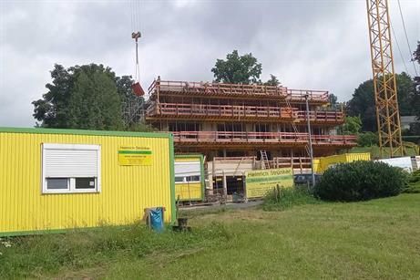 Ein großes im Bau befindliches Gebäude mit einem gelben Gebäude im Vordergrund und einem Kran im Hintergrund.
