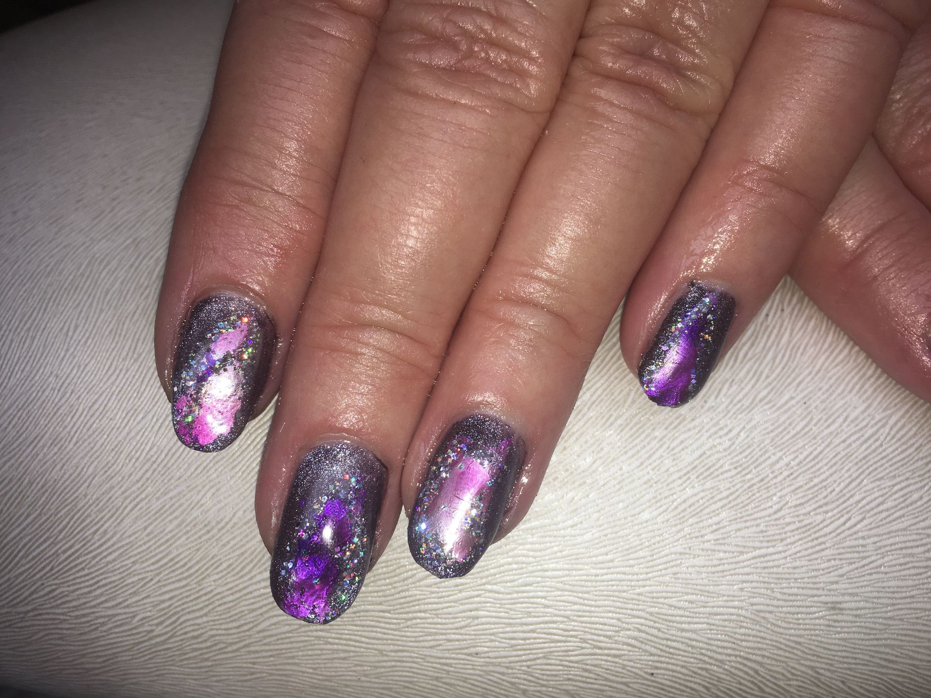 Dunkle Glitzer-Maniküre mit lila und pinkem Schimmer auf mandelförmigen Nägeln mit Metallic-Effekt.