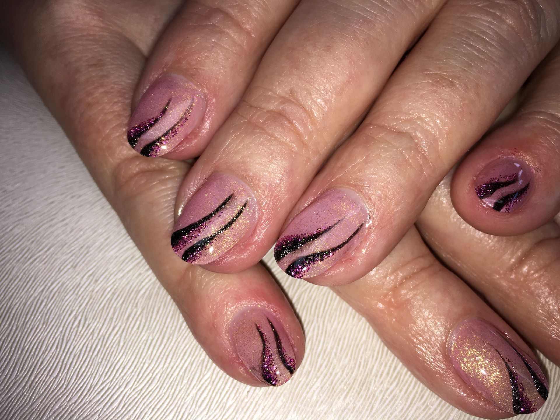 Rosa Maniküre mit schwarzen Glitzerlinien im modernen Wellen-Design auf kurzen, rund gefeilten Nägeln.