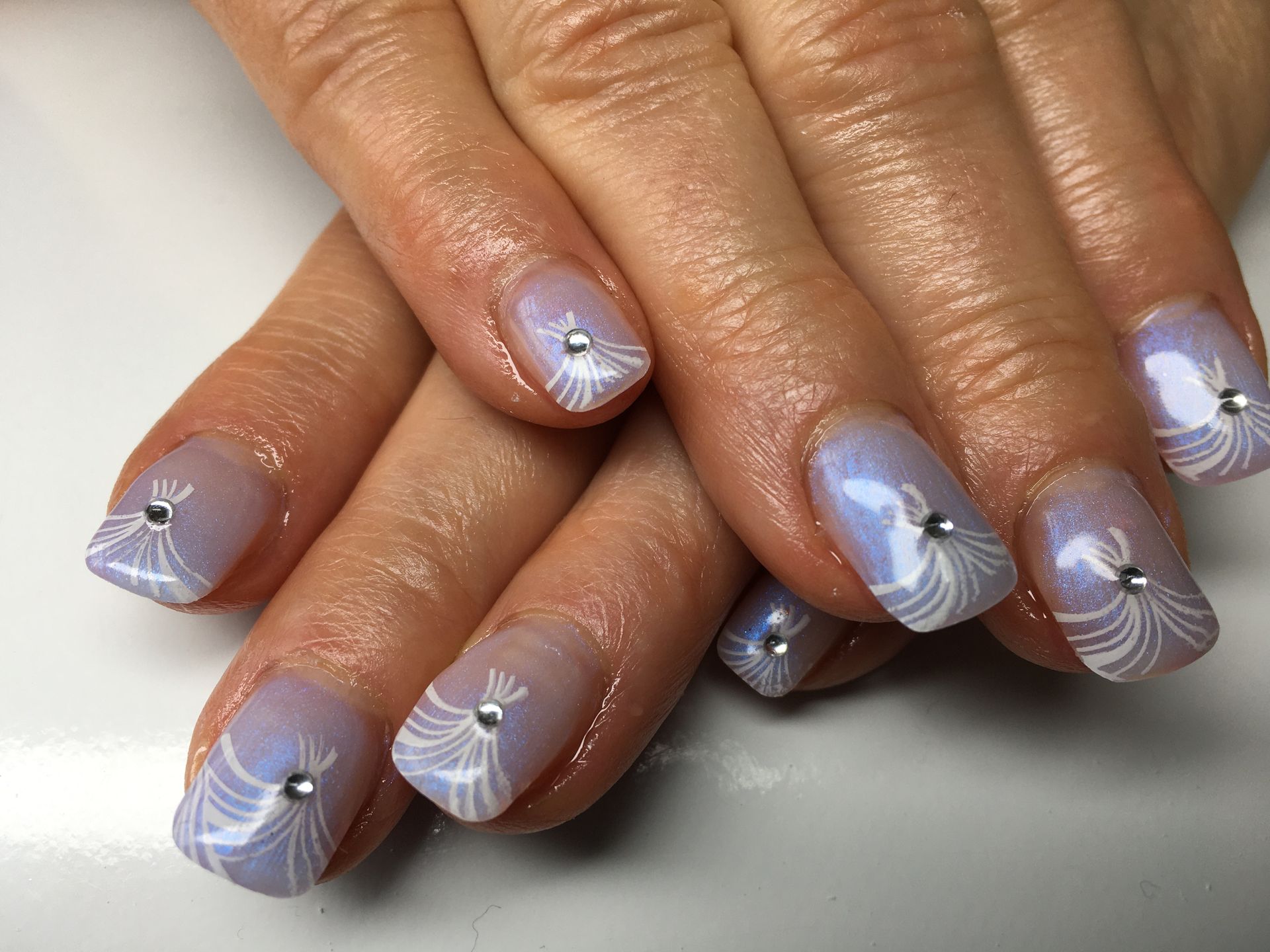 Lila Maniküre mit feinem Linien-Nailart und kleinen Strasssteinen auf mandelförmigen Nägeln.