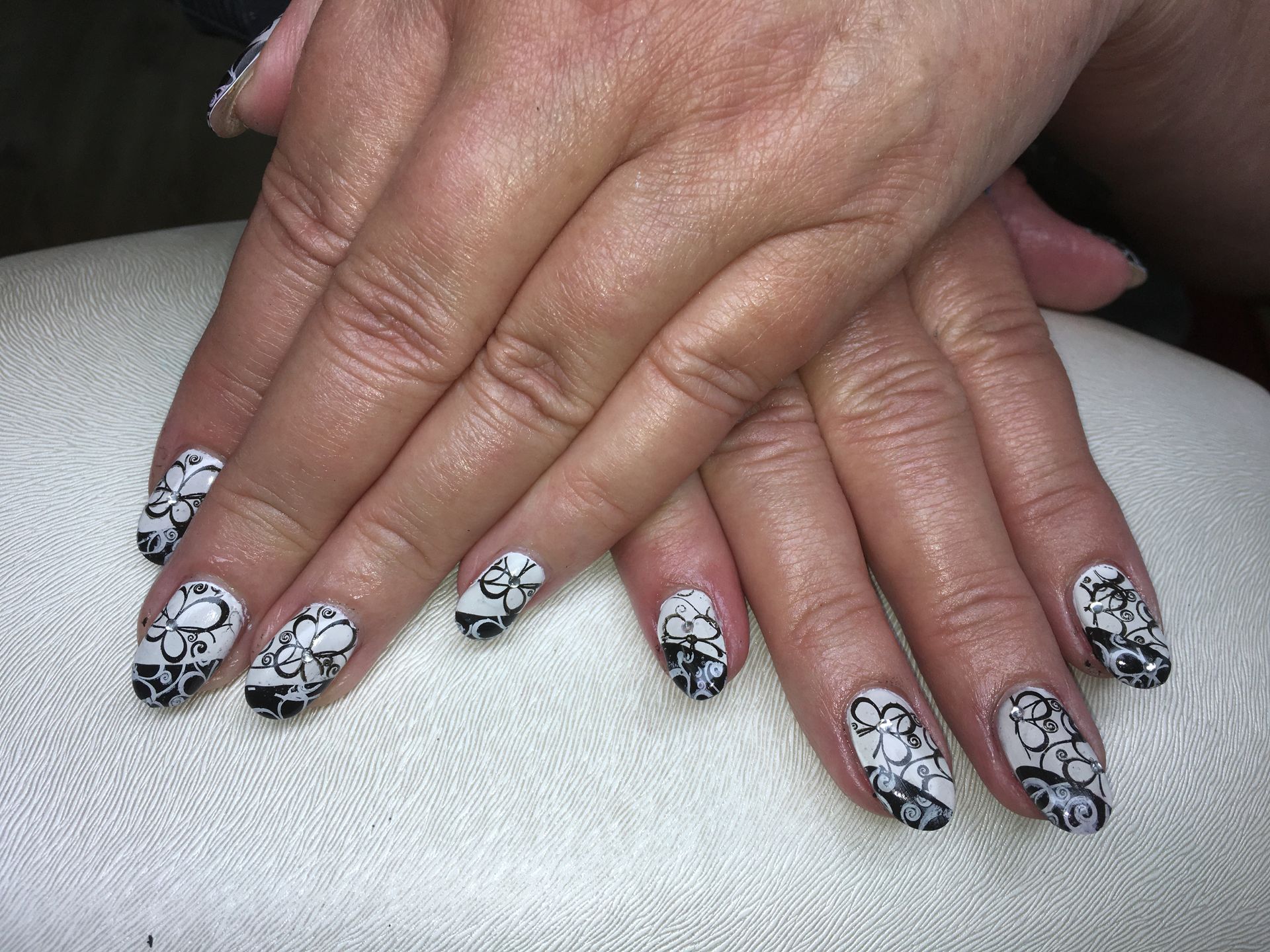 Schwarz-weiße Maniküre mit floralem Nailart-Muster auf kurzen Nägeln mit glänzendem Gel-Look.